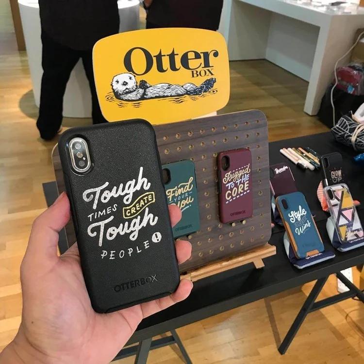 Custom hand-lettered OtterBox phone cases displayed at an event