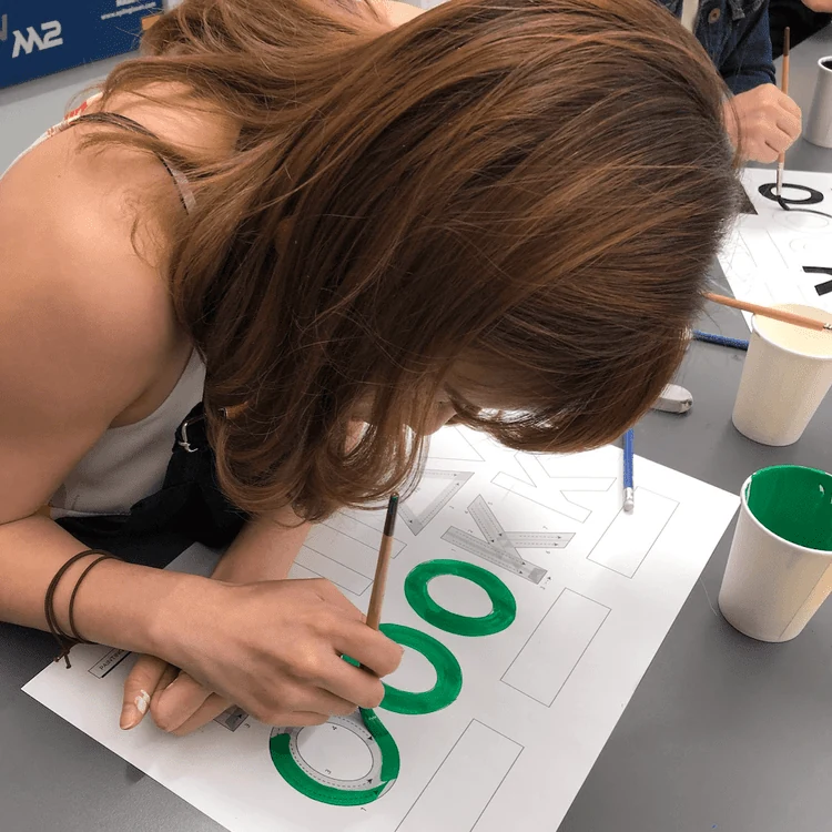 Participant painting letters during a sign-painting class